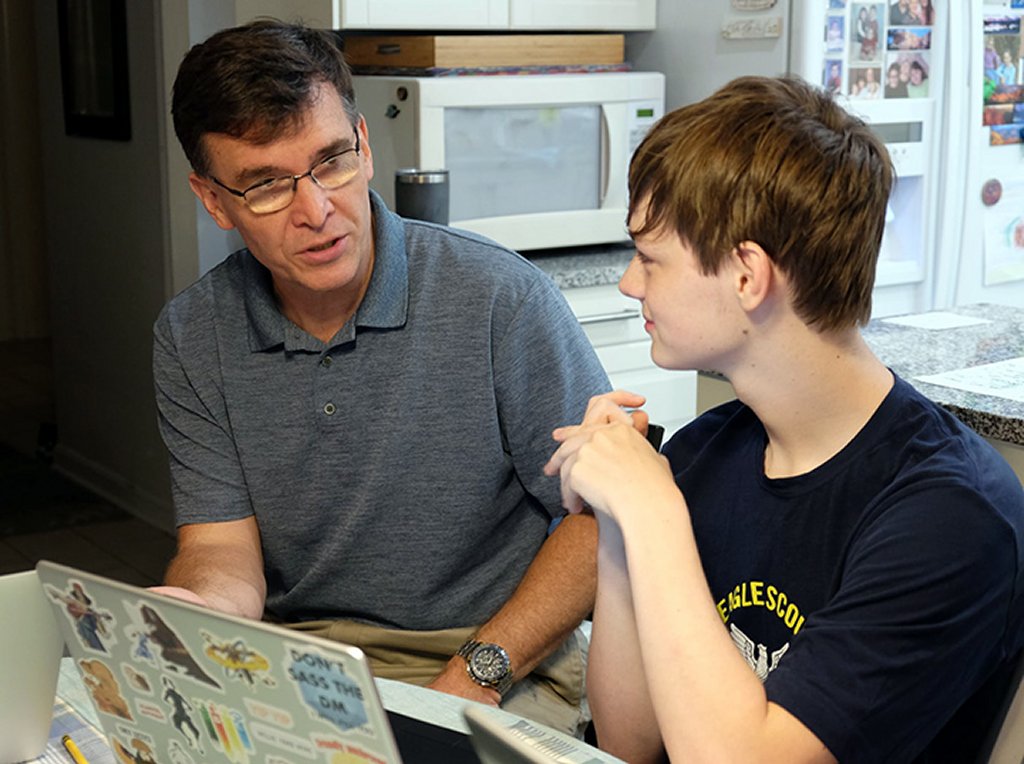 Dan Ensminger, left, head coach of the Bot Brigade Quartic robotic team, discusses robot programming with team member, Seth Rollins. For the past 14 years, Ensminger has opened his home to the local youth teams, providing them with a positive environment to learn problem-solving and practical applications. (Photo courtesy of Bot Brigade Quartic)