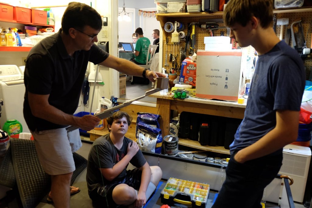 Dan Ensminger, left, head coach of the Bot Brigade Quartic robotics team, explains a practical application of building robotics to two team members in his garage, while other team members work out 3D modeling around from his kitchen table. Ensminger has led local Bot Brigade teams for the past 14 years. (Photo courtesy of Bot Brigade Quartic)