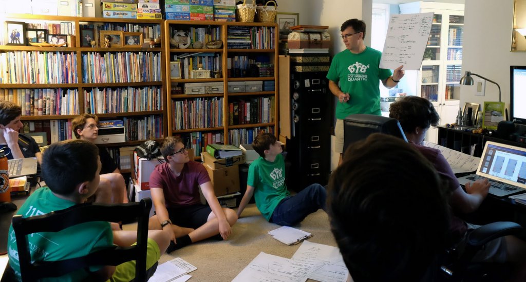 Dan Ensminger, standing, head coach of the Bot Brigade Quartic robotic team, tries to make learning fun while facilitating a robot design review. For the past 14 years, Ensminger has opened his home to the local youth teams, providing them with a positive environment to learn problem-solving and practical applications. (Photo courtesy of Bot Brigade Quartic)